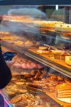 Dessert display case shows cheesecakes, pastries, cookies, and sliced cake on trays behind glass in cafe. Dessert selection for bakery menu, retail food service, catering, takeaway, and shop marketing