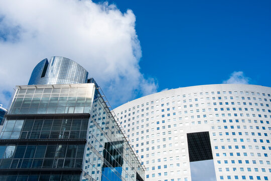 A glass facade and sweeping curve join towers in an urban skyline of Paris, France, where architecture rises into a bright sky