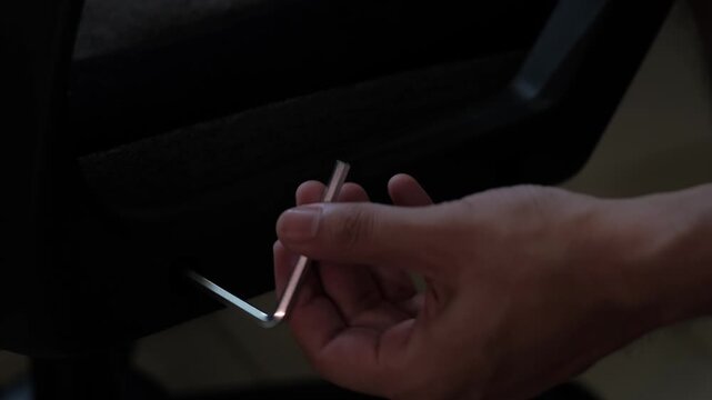 Close-up static shot of hands using an allen wrench to tighten a gaming chair base during furniture assembly indoors