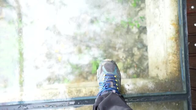 First person perspective of a person walking on a transparent glass skywalk high in the mountains