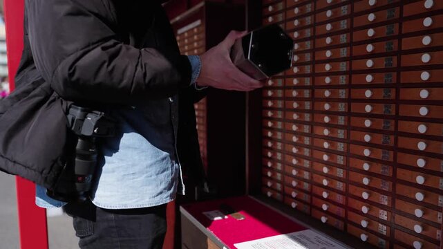 Male tourist with camera pulling fortune stick from omikuji wooden drawer cabinet at outdoor shrine Tokyo Japan