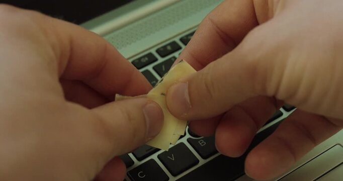 Close-up of hands tearing a paper note above a laptop keyboard, symbolizing password security, data protection, privacy, and avoiding unsafe password storage.