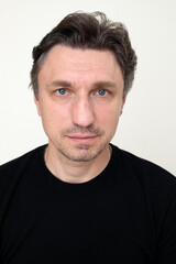 Fototapeta premium close up portrait of serious middle aged man with blue eyes and stubble in black t-shirt looking directly at camera, white background headshot