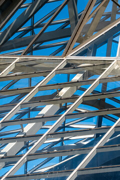 Steel trusses cross a modern building glass facade beneath blue sky, shaping urban architecture into abstract geometry, pattern and structural detail