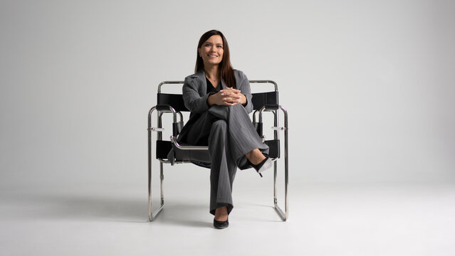 Portrait of a cheerful young businesswoman sitting in a chair against white background.
