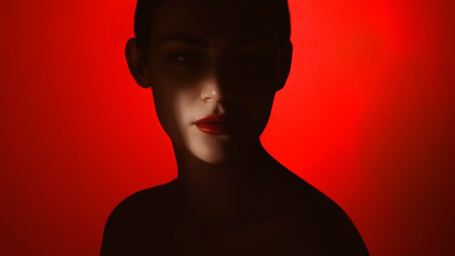 Dramatic beauty portrait of calm woman with red lips in shadow on red background. Concept of luxury lipstick campaign, mysterious beauty editorial, premium skincare and perfume advertising.