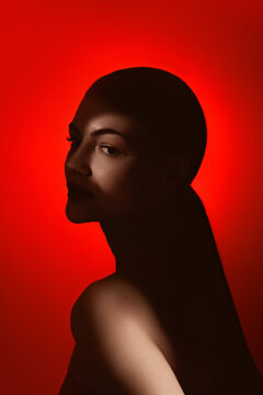 Side beauty portrait of serene woman in dark silhouette on red background. Concept of high end skincare promo, elegant haircare campaign, fragrance launch and dramatic fashion branding.