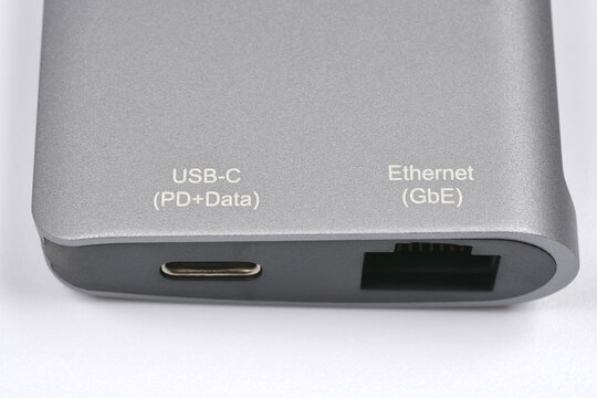 Close up view of a grey aluminum USB-C hub showing a USB-C port and a Gigabit Ethernet port with printed text labels.