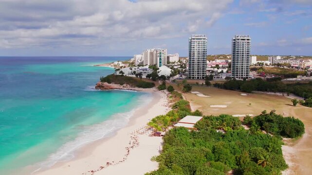 Aerial bird's-eye view of Simpson Bay beach, St. Martin, showcasing the white sandy shoreline, tropical resorts, and gentle turquoise waves during a bright sunny day.
