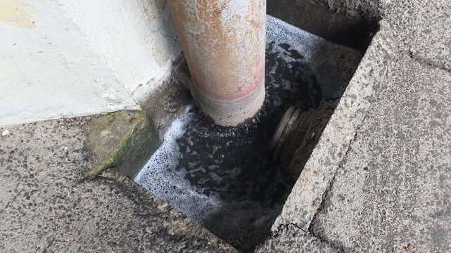 Drain pipe releasing murky water with foam into a concrete gully, showing environmental concerns, urban pollution, and potential industrial wastewater runoff