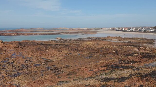 Cobo Bay Guernsey Channel Islands slow forward drone flight over pink granite rock formations with golden sandy beaches calm sea in late afternoon sun with views of seafront properties and coast
