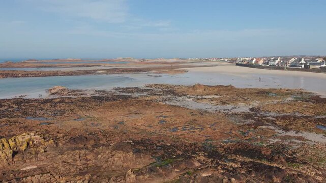 Cobo Bay Guernsey Channel Islands forward drone flight over pink granite rock formations with golden sandy beaches calm sea in late afternoon sun with views of seafront properties and coast