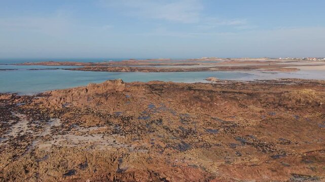 Cobo Bay Guernsey Channel Islands Reveal of pink granite rock formations and sandy beaches with calm sea in late afternoon sun pulling back to view of the bay through old pine tree