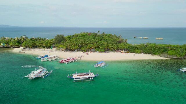Aerial lateral view of Crystal Cove Island in Boracay captures colorful bangka outrigger boats actively arriving and departing from its white sandy beach