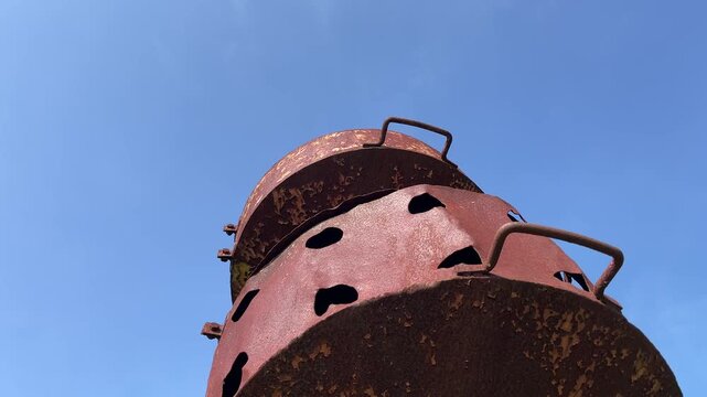 Extreme low-angle view of rusty ancient warning siren under blue sky in rural Asia with dramatic nostalgic atmosphere and historical relic concept.