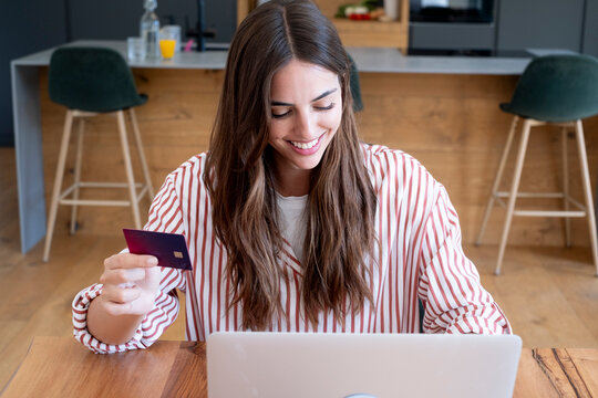 Young woman smiling while making an online purchase on a laptop with a credit card at home