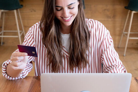 Smiling woman paying with credit card on laptop while working or shopping from home