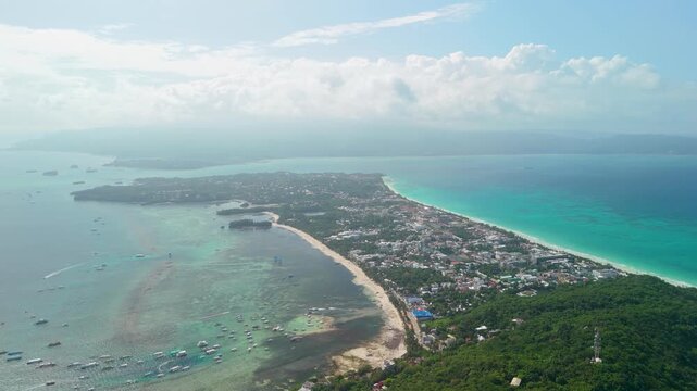 High-altitude aerial cityscape of Boracay Island reveals Bulabog Beach, Habagat Bay, dense resort town, turquoise Sulu Sea and dozens of boats moored in calm waters