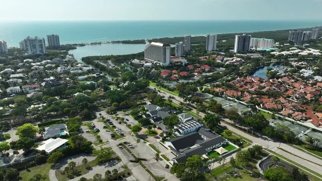 Aerial drone view of Naples United Church of Christ in Naples, Florida, surrounded by lush palm trees, residential neighborhoods, and the sparkling Gulf coast in the distance.