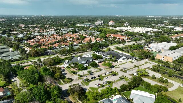 Cinematic bird's-eye shot of the Naples United Church of Christ, framed by upscale Florida homes, tree-lined streets, and the distant Naples skyline along the Gulf.