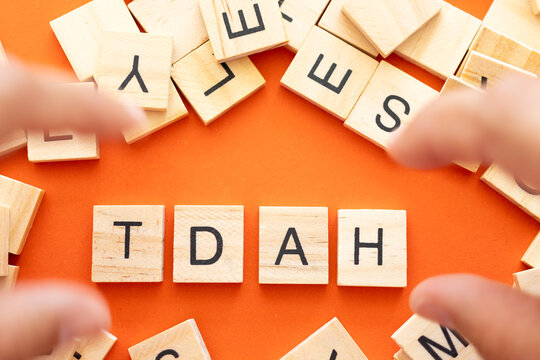 Hands in motion over wooden letters spelling out Wooden tiles spelling TDAH on an orange background 