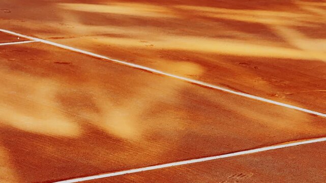 Sunlit clay tennis court with crisp white boundary lines, highlighting warm orange texture, soft shadows, and the calm geometry of an empty sports venue.