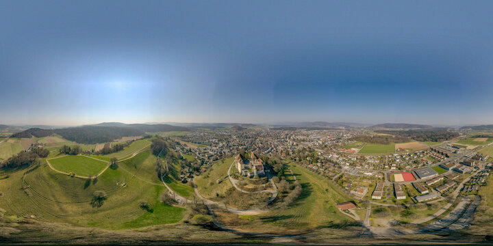 Aerial view of Lenzburg Castle on a hilltop overlooking the town, green fields, and forests under a clear blue sky Lenzburg, Aargau, Switzerland.