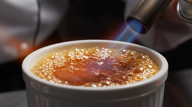 Chef Using Blowtorch to Caramelize Sugar on Creme Brulee in White Ramekin
