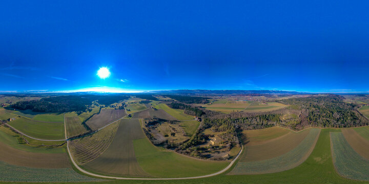 Aerial view of the Seeland District featuring vast agricultural fields and dense forests under a bright sun in Grossaffoltern, Bern, Switzerland.
