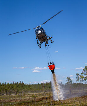 Helicopter pouring water with bucket on land while flying against blue sky