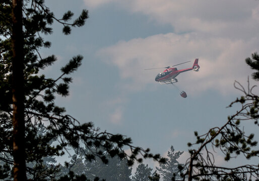 Low angle view of helicopter carrying water bucket for extinguishing fire while flying in sky