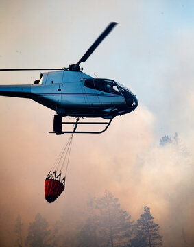 Helicopter carrying water bucket for extinguishing forest fire while flying in sky