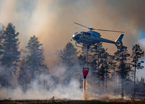 Helicopter pouring sand down with bucket on land against smoky sky and trees