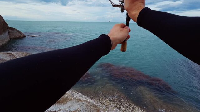 First Person View of Fisherman Reeling Spinning Rod and Playing Artificial Lure Above Tropical Sea Near Rocky Coastline, Recreational Saltwater Fishing