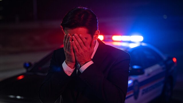 Man covering face near police car at night