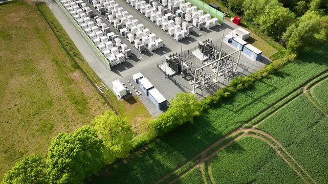 Aerial footage of utility-scale battery energy storage system (BESS) with rows of battery containers, electrical substation infrastructure, and grid connection equipment.