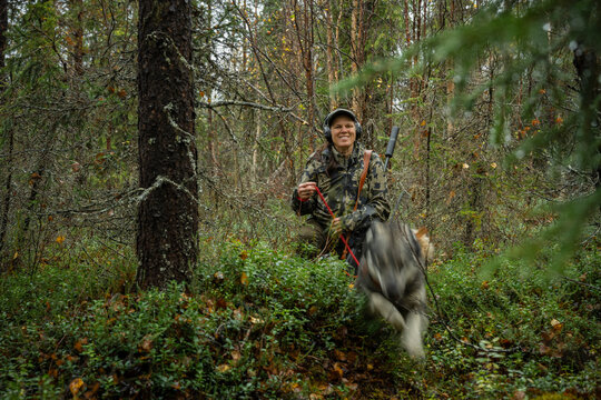 Smiling woman with hunting dog jumping over bushes in forest
