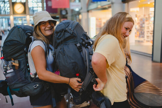 Happy female tourists with backpacks standing at railway station