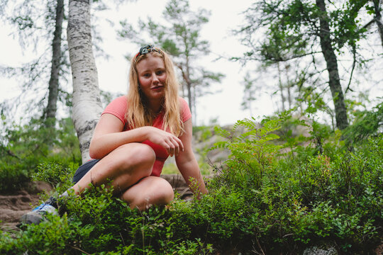 Portrait of woman with blond hair sitting amidst plants in forest