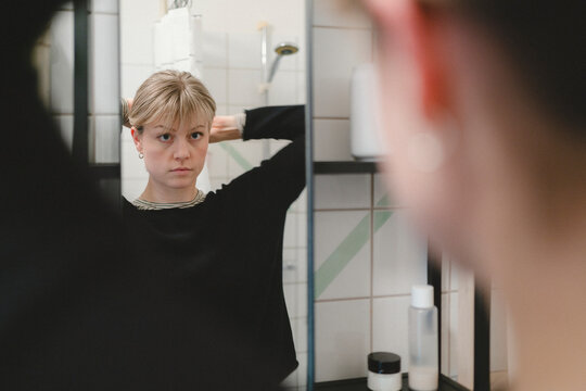 Woman tying her hair while looking in bathroom mirror