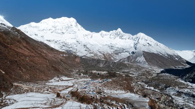 A panoramic aerial view of the snow-covered Manaslu massif towering above a village in the valley below in Nepal.
