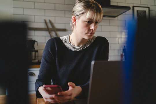 Female freelancer doing multi-tasking with smart phone and laptop while working from home