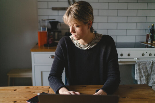 Businesswoman checking notifications on her smart phone while working on laptop at home