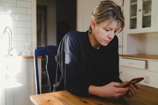 Woman scrolling smart phone while sitting at dining table in home