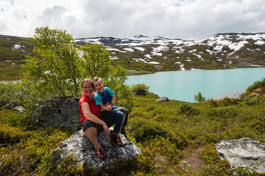 Smiling woman sitting with her son on rock near lake