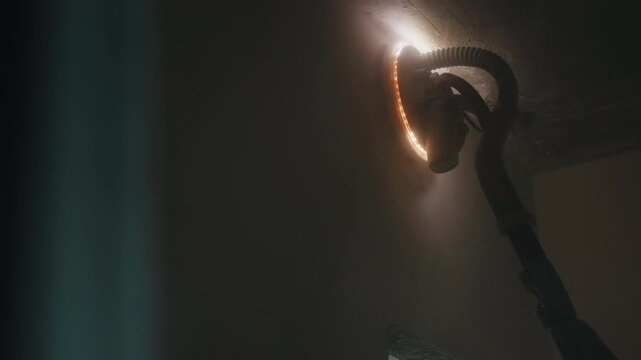 Worker sanding interior wall with illuminated drywall sander close up