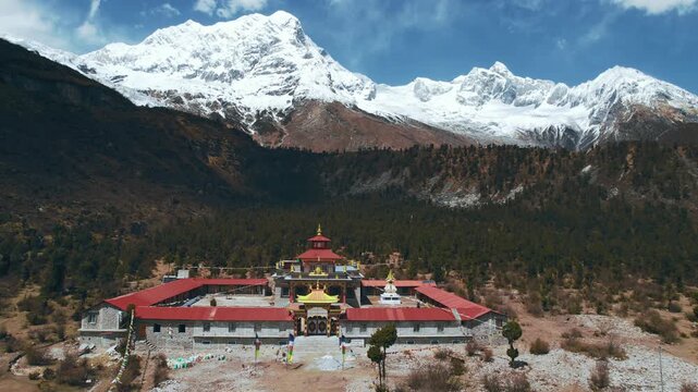 An aerial view of a large Buddhist monastery with red roofs set in a valley below the towering snow-capped Manaslu massif in Nepal.