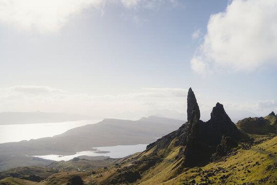 Rugged green slopes and ancient rock formations overlooking bright sky during daytime