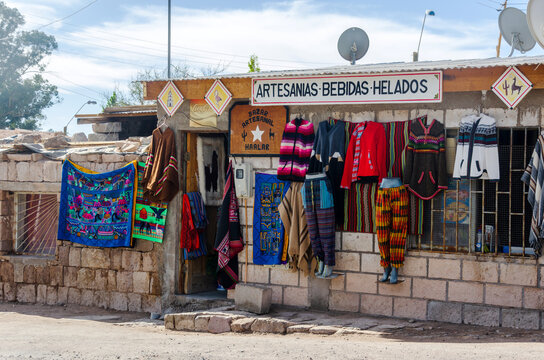 Handmade Andean textiles and clothing hang outside a rustic stone artisan shop in northern Chile