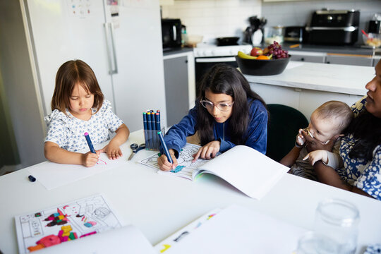 High angle view of girls coloring while sitting with mother and toddler brother at table in home